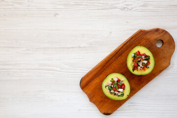 Homemade Pico de Gallo Stuffed Avocado on a rustic wooden board on a white wooden surface, top view. Flat lay, overhead, from above. Copy space.
