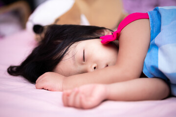 Obraz na płótnie Canvas Asian child is sleeping on a pink bed. Kid covers the cloth with a blue blanket. Children sleep sweetly. Adorable children rest and sleep in the afternoon. Baby aged 3 years and 5 month.