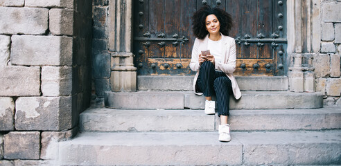 Black tourist with smartphone resting on stone steps