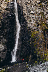 Obraz premium noise effect, selective focus: miniature tourist dressed in a bright colored raincoat that is contrastingly visible on a large scale background of a cliff with a waterfall