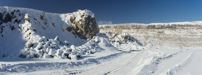 Panorama of the relief in a stone quarry covered with snow in a winter sunny day.