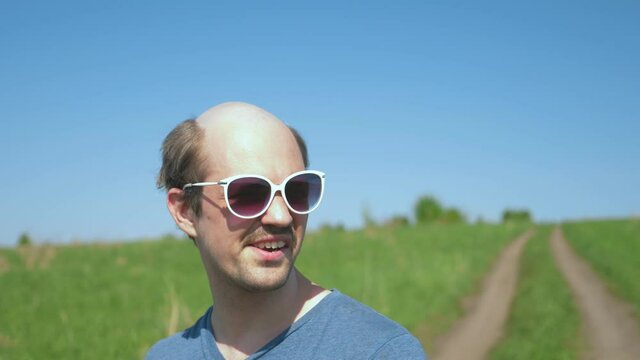 portrait. cheerful bald guy in sunglasses in the field on a clear sunny day