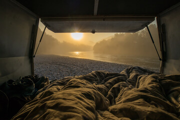 View from a bed in the vintage campervan parked on the shores of a river in early morning hours....