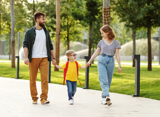 Full body cheerful mother and father holding hands with smart schoolboy and communicating while...