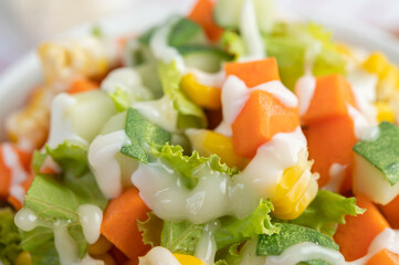 Cucumber salad, corn, carrot and lettuce in a white cup.