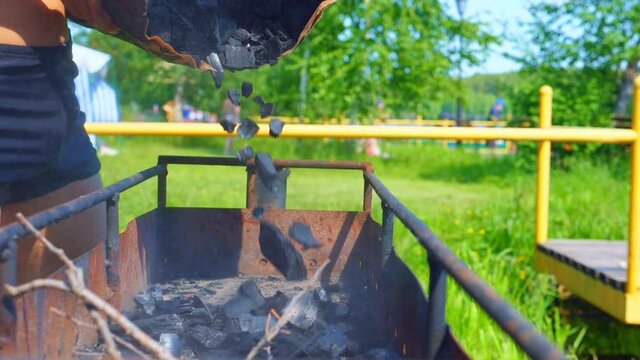 A young man adds coals into a old rusty brazier. Friends are going to have a barbecue outdoors. Slow motion