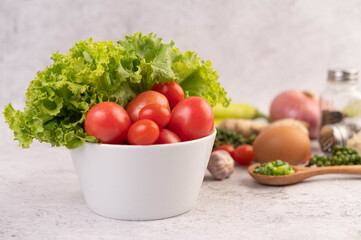 Lettuce and tomatoes in a white cup with sliced ​​onions and fresh peppers on the cement floor.