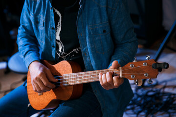 A young man plays the guitar while sitting. Ukulele game