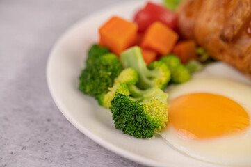 Breakfast consisting of bread, fried eggs, broccoli, carrots, tomatoes and lettuce on a white plate.