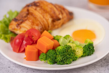 Breakfast consisting of bread, fried eggs, broccoli, carrots, tomatoes and lettuce on a white plate.