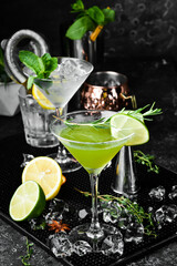 Green alcoholic cocktail with lime and rosemary. On a black stone background. Menu bar.