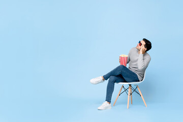 Young Caucasian man with popcorn and 3d movie glasses looking at empty space while sitting on chair...
