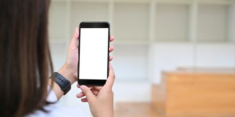 Behind of woman is holding a white blank screen smartphone while standing over blurred background.