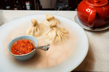 Juicy khinkali on a white plate. Served with sauce. Traditional dish. Wooden serving tray inculami is on the plate, which poured water that soars.