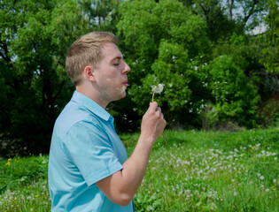 A young guy blowing on a dandelion blossom. Interesting summer fun.