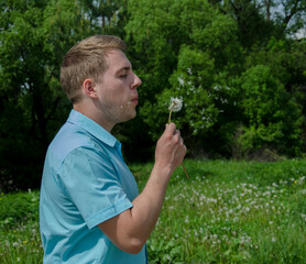 A young guy blowing on a dandelion blossom. Interesting summer fun.