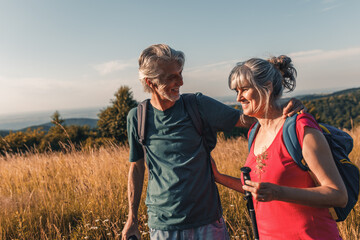 Active senior couple hiking in nature with backpacks, enjoying their adventure at sunset.