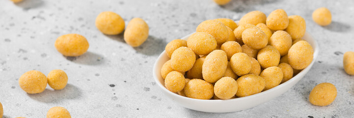Fried peanuts in cheese sauce in a white bowl on a light gray table. Banner with space for text