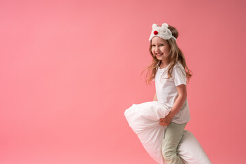 charming little girl in a sleep mask and pajamas jumps and flies on pillows