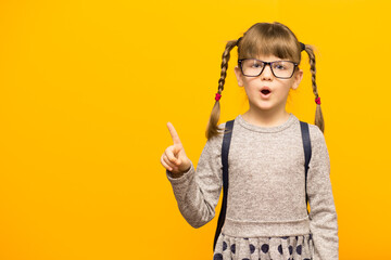 Portrait of stylish child girl pointed finger up. Little child in glasses has idea. Kid isolated on yellow background.