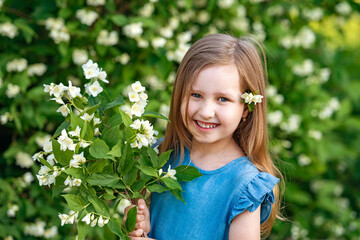 charming little girl 4 years old sniffs Jasmine flowers in Sunny summer garden