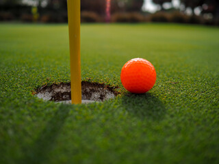 The orange golf ball that is about to pour into the hole.
