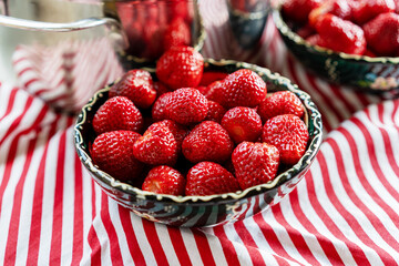 Strawberries bowl, pot on stripped red white background. Colourful kitchen background, summer vibes.