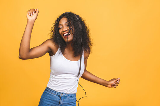 Studio photo of inspired african american lady listening music, dancing with eyes closed. Indoor portrait of relaxed black girl isolated on yellow background.