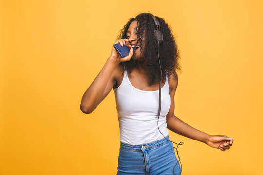 Studio photo of inspired african american lady listening music, dancing with eyes closed. Indoor portrait of relaxed black girl isolated on yellow background.