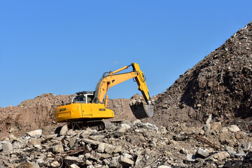 Fototapeta na wymiar Yellow excavator at landfill for disposal of construction waste. Backhoe dig gravel at mining quarry on blue sky background. Recycling concrete and asphalt from demolition.