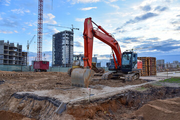 Excavator during earthmoving at construction site on bluue sky background. Сonstruction machinery for excavating. Tower cranes lifting a concrete bucket for pouring of concrete into formwork