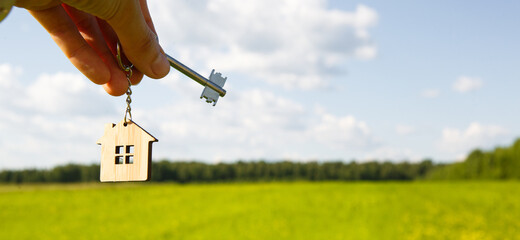 Wooden pendant of a house and key. Background of the sky and field. Dream of home, building a...