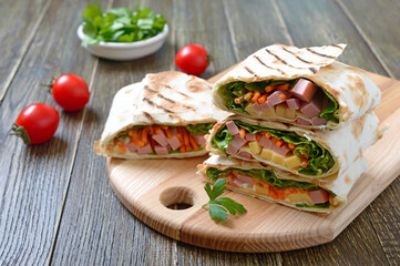 Lavash rolls with vegetables, ham and cheese. Tasty breakfast appetizer on a wooden board.