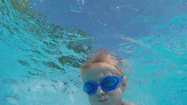 Young boy in swimming goggles jumps underwater into a pool
