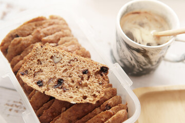 Closeup of delicious looking, fluffy and moist banana bread slices in airtight container and a cup of coffee on wooden table. Healthy breakfast, brunch and dessert. 