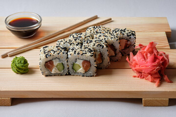 Japanese sushi rolls named Manhattan  with sesame wasabi, soy sauce, basil leaves and marinated ginger. Tasty and artistic food for restaurant or cafe menu. Roll on the wooden board.