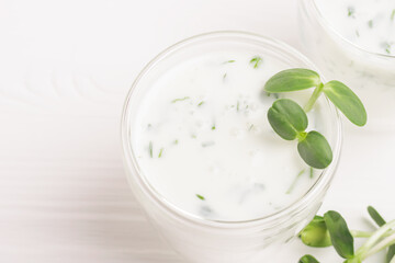 Green smoothie milkshake with the addition of fresh microgreen herb sprouts in a glass beaker on a white background.