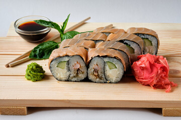 Japanese sushi rolls with Salmon, wasabi, soy sauce, basil leaves and marinated ginger. Tasty and artistic food for restaurant or cafe menu. Roll on the wooden board. Food photography.