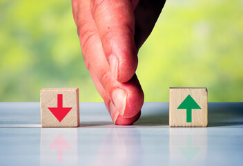 The hand separates two wooden blocki with red arrow down and green arrow up. Symbol for the...