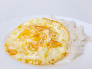 Fried egg or overcooked sunny side up, served with white rice, on a white plate, isolated in white background