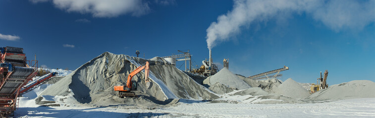 Excavators and stone crushing equipment of mining and processing plant on the background of a blue...