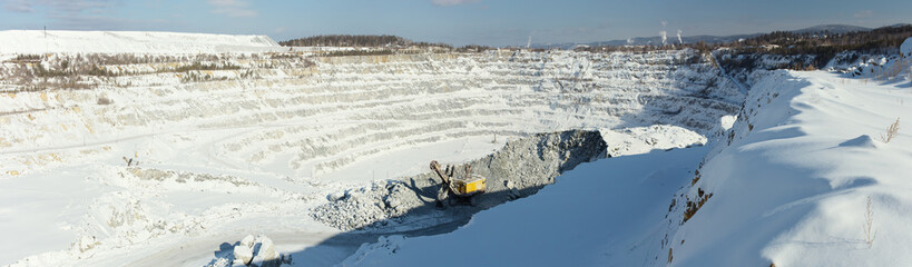 Huge snow-covered quarry for the extraction of limestone and an excavator in the foreground, panoramic image.