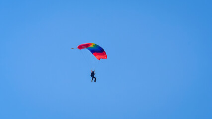 Skydiver and colorful parachute on the blue sky 