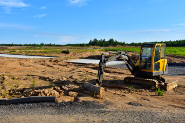 Mini excavator digg trench to lay cables concrete curbs and paving slabs at construction site. Backhoe on earthwork/roadworks © MaxSafaniuk