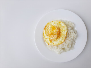Fried egg or overcooked sunny side up, served with white rice, on a white plate, isolated in white background