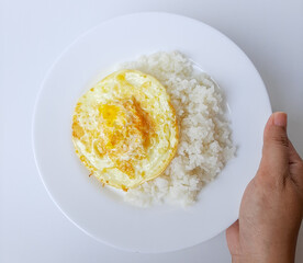 Fried egg or overcooked sunny side up, served with white rice, on a white plate, isolated in white background