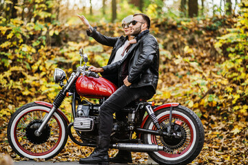 Obraz na płótnie Canvas Pretty couple near red motorcycle on the road in the forest with colorful blured background