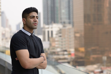 Portrait of young handsome Indian man thinking with arms crossed in the city