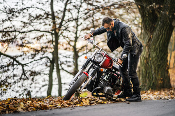 Bearded brutal man in sunglasses and leather jacket sitting on a motorcycle on the road in the...