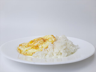 Fried egg or overcooked sunny side up, served with white rice, on a white plate, isolated in white background